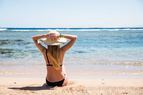 Mulher bonita com as mãos levantadas sentado feliz na areia na praia — Fotografia de Stock