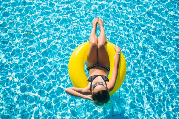 Glückliche junge Frau im Bikini mit aufblasbarem Schwimmer aus Gummi, die an einem sommerlich heißen Tag spielt und sich am Pool vergnügt — Stockfoto