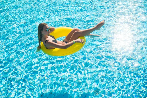 Frau entspannt sich auf Donut-Gelb im Poolwasser an heißen, sonnigen Tagen. Sommerferienidylle. Ansicht von oben. — Stockfoto