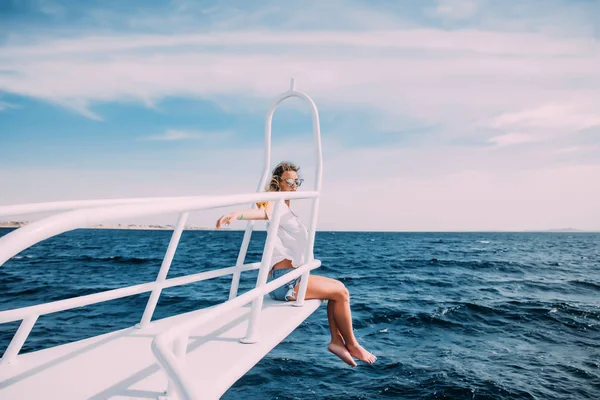 Hermosa mujer en traje de baño blanco de pie en la nariz del yate y separar las manos en un día soleado de verano, brisa que desarrolla el pelo, hermoso mar turquesa en el fondo —  Fotos de Stock