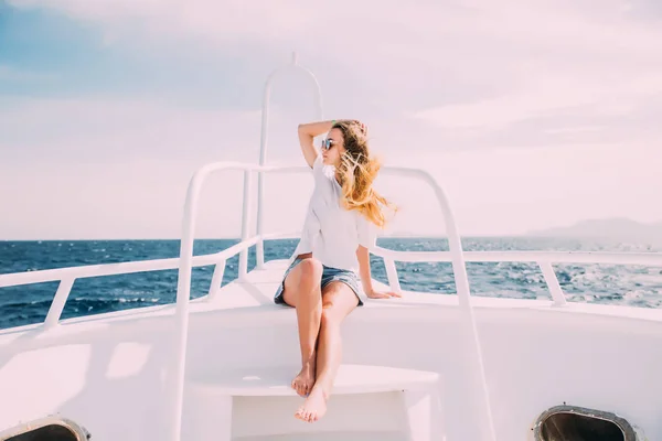 Vidám fiatal nő támaszkodva, a korlát, és mosolyogva kamera állva a hajó orr — Stock Fotó