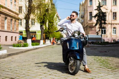 Scooter üzerinde oturan ve cep telefonda konuşurken neşeli genç adam