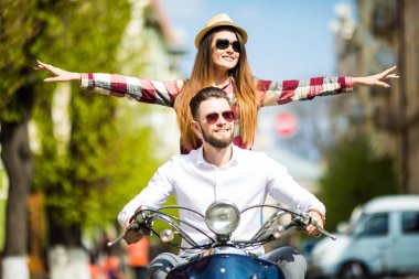 Güzel genç çift sürme scooter silah yükseltmek ve gülümseyen mutlu kadın birlikte