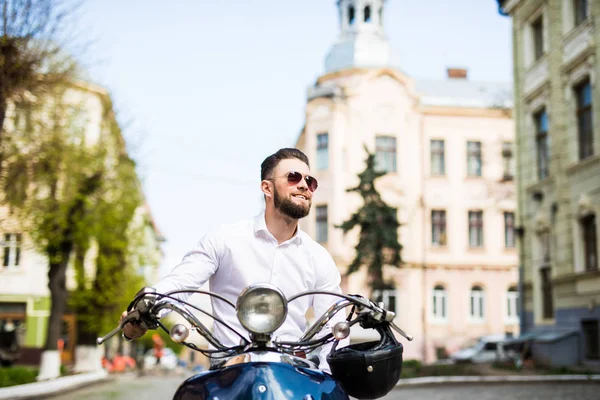 Молодой человек в солнечных очках катается на скутере по улицам города — стоковое фото