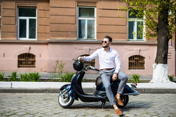 Стильний модний чоловік у сучасних сонцезахисних окулярах та офіційний костюм, що сидить на мотоциклі на вулиці міста — стокове фото