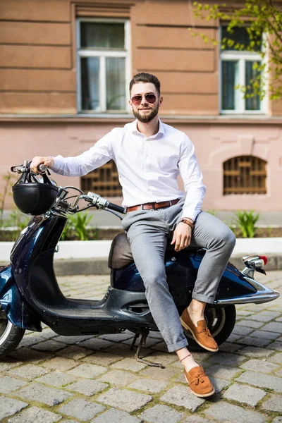 Elegante homem na moda vestindo óculos de sol modernos e um terno formal sentado esperando em uma motocicleta na rua da cidade — Fotografia de Stock