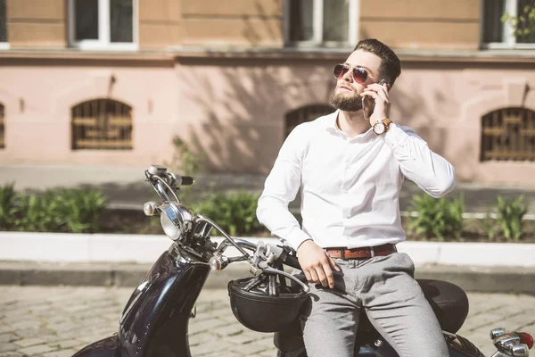 Jovem sentado em scooter e usando telefone inteligente na rua da cidade — Fotografia de Stock