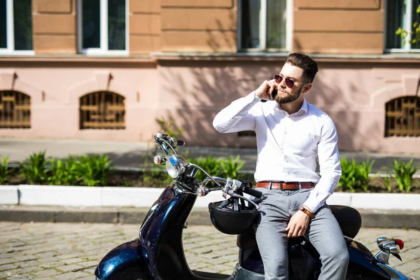 젊은 남자 스쿠터에 앉아 및 거리에 스마트 휴대 전화를 사용 하 여 — 스톡 사진