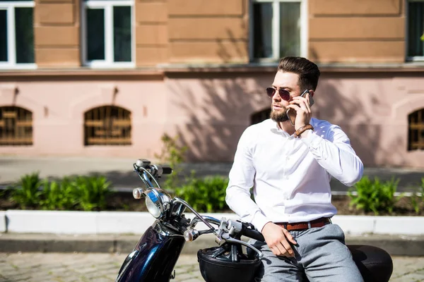 Красавчик, сидящий на мотоцикле и разговаривающий по телефону на городской улице. — стоковое фото