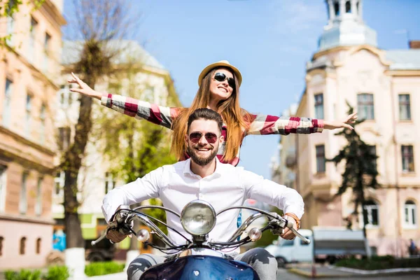 Bonito jovem casal montando scooter juntos enquanto mulher feliz mantendo os braços estendidos e sorrindo — Fotografia de Stock