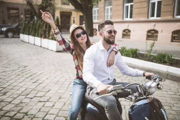 Belo jovem casal montando scooter ao longo de uma rua e sorrindo. tonificado — Fotografia de Stock