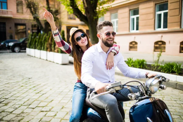 Beautiful young couple riding scooter along a street and smiling