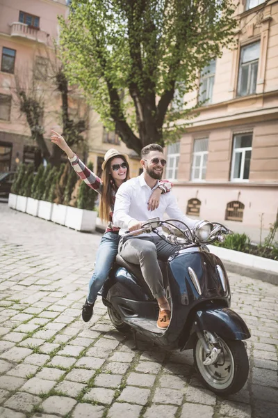 Belo jovem casal montando scooter ao longo de uma rua e sorrindo — Fotografia de Stock