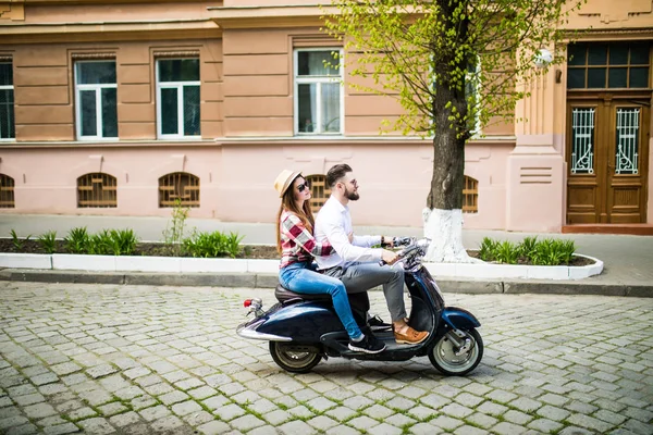 Alegre jovem casal montando uma scooter na rua da cidade com diversão — Fotografia de Stock