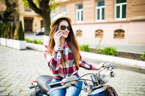오토바이에 앉아있는 동안 스마트폰 사용 하 여 모자에 아주 젊은 여자. — 스톡 사진
