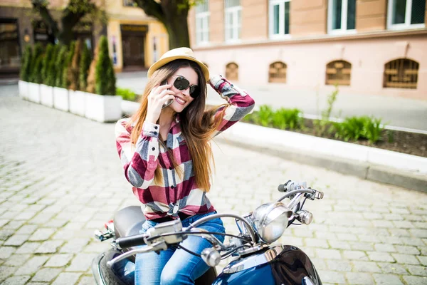 Mulher bonita no chapéu usando smartphone enquanto sentado em moto . — Fotografia de Stock