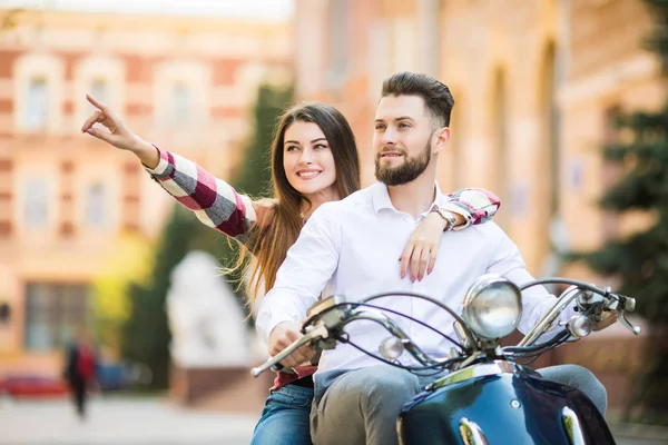 Beautiful young couple riding scooter together while happy woman pointing away and smiling — Stock Photo, Image