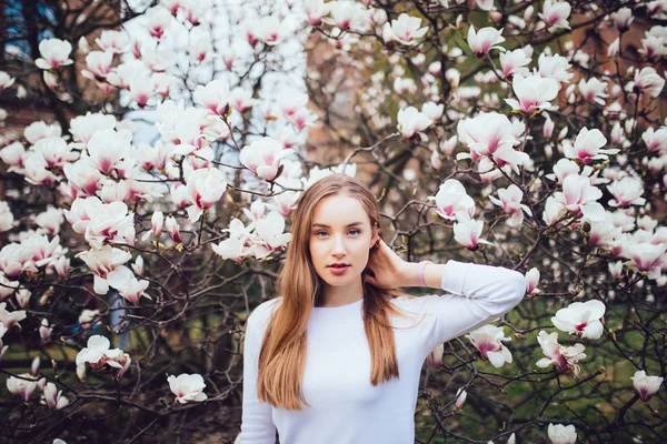 Mulher de beleza em pé no fundo Magnolia flores florescentes, mãos na cabeça . — Fotografia de Stock