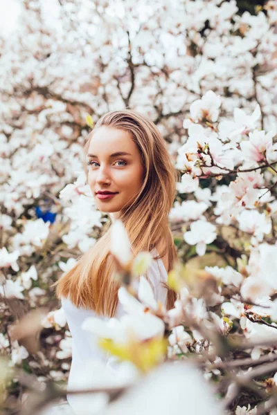 Bella giovane donna bionda circondata da fiori di magnolia nel giardino primaverile — Foto Stock