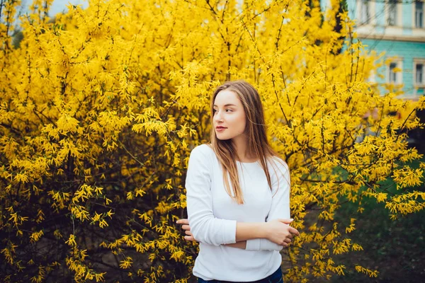 Donna in piedi di fronte all'albero giallo in fiore in strada in primavera — Foto Stock