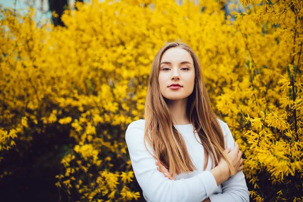 Женщина, стоящая перед желтым цветущим деревом на городской улице — стоковое фото