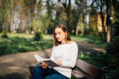 Üniversite öğrencisi parkta bankta oturan bir kitap okuma