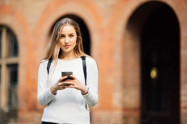 Hermosa estudiante feliz sosteniendo portátiles mensajes de texto en el teléfono en la Universidad — Foto de Stock