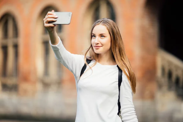 Dziewczyna student college'u, siedząc na zewnątrz budynku i biorąc selfie na tle campus — Zdjęcie stockowe
