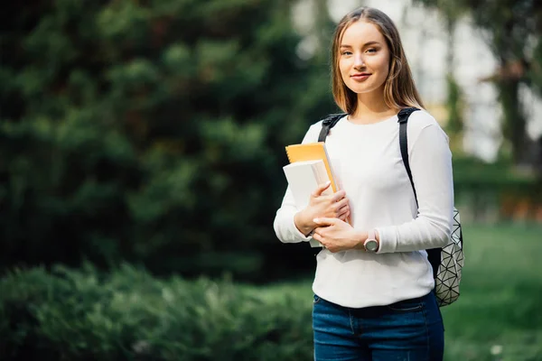 Estudante retrato menina segurando livros usando mochila ao ar livre no parque sorrindo feliz voltar para a escola. branco jovem mulher modelo . — Fotografia de Stock