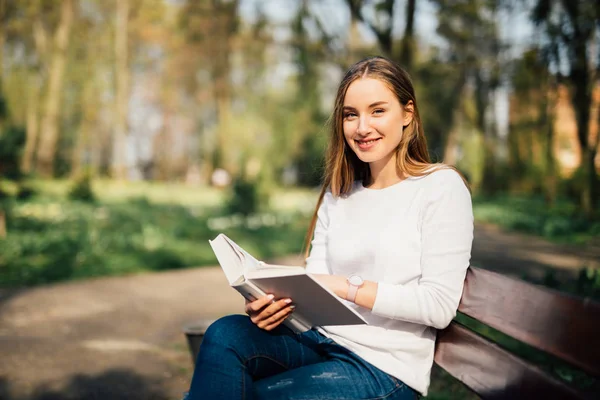 Estudante universitário lendo um livro no parque sentado no banco — Fotografia de Stock