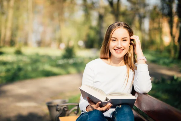 Estudante universitário menina ler um livro sentado no banco no parque da cidade — Fotografia de Stock