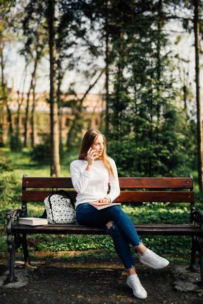 Молодая студентка пользуется смартфоном, сидя на скамейке в парке . — стоковое фото