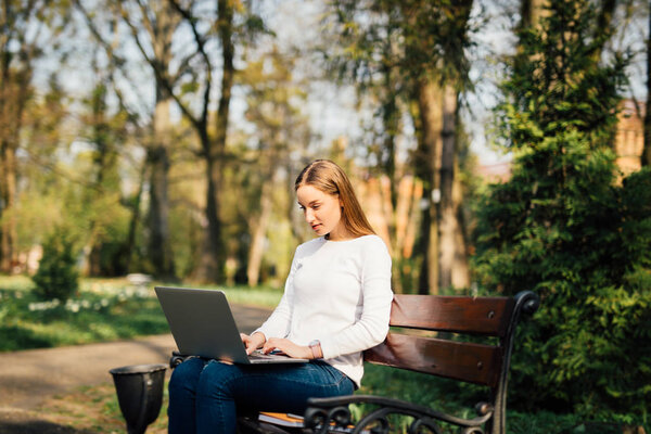Young girl on a bench with a laptop in park