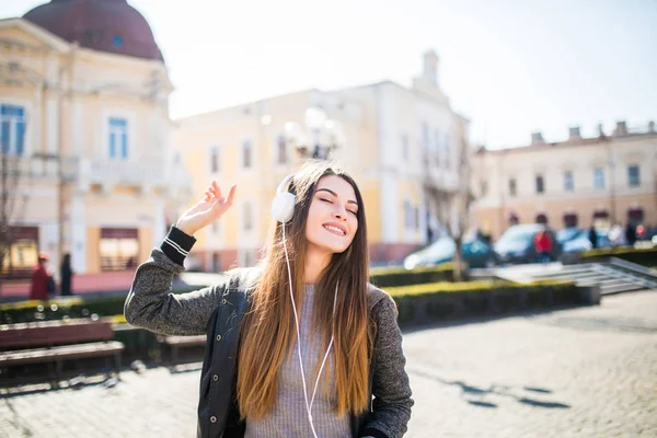 Mujer sonriente con auriculares escuchando música en la calle . — Foto de Stock