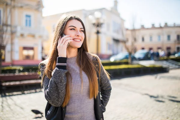Beautiful young brunette woman speaking on the smart-phone at the city street background. — Stock Photo, Image