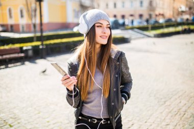 Kadın hatta yaz güneşli bir gün sokakta bir akıllı telefon üzerinden kablosuz kulaklık ile müzik dinleme