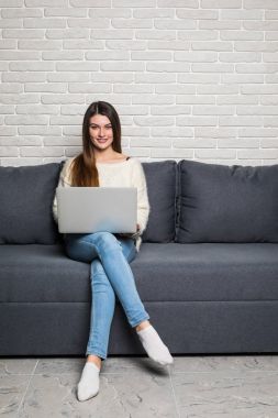 Happy pretty woman using laptop sitting on cosy sofa at home clipart