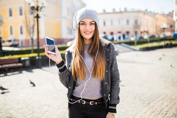 Joyful woman listening songs from phone and feeling music in the street at sunset with a warm sunlight in the background — Stock Photo, Image