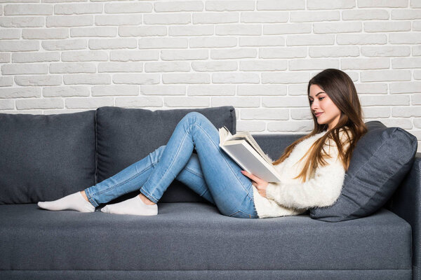 Happy young woman reading storybook on couch at home