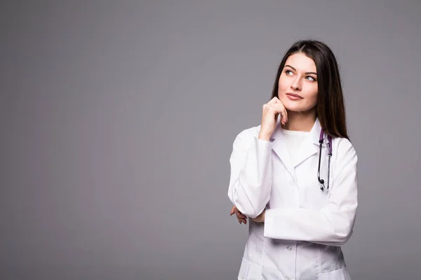 Meditada, Doctora joven mirando hacia otro lado aislada sobre fondo gris — Foto de Stock