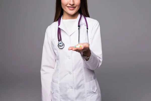 Glad ung kvinna läkare med stetoskop visar piller i hennes hand som isolerad på grå — Stockfoto