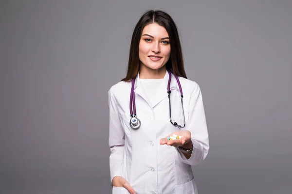 Jovem médica alegre com estetoscópio mostrando pílula na mão isolada em cinza — Fotografia de Stock