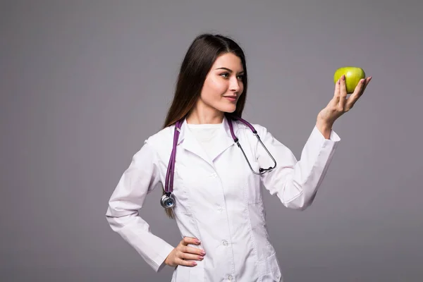 Alegre linda joven médico de pie y sosteniendo una manzana sobre fondo gris — Foto de Stock