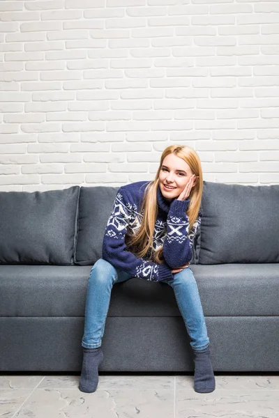 Blond kobieta siedzi na jej białej kanapie w domu — Zdjęcie stockowe