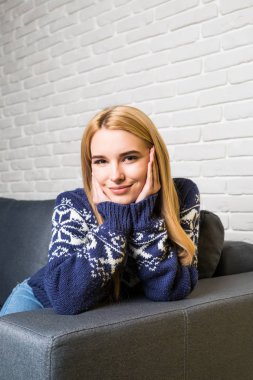 Kameraya bakarak ve evde kanepede otururken gülümseyen güzel mutlu kadın portresi yakın çekim