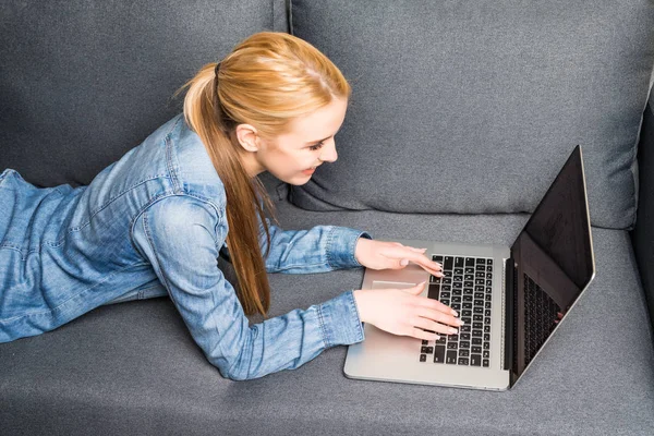 Casual jeune femme couché sur le canapé et en utilisant un ordinateur portable à la maison — Photo