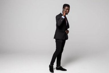 Tam yükseklikte kendine güvenen genç Afrika adam cep telefonu gri arka plan karşı dururken konuşurken