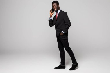 Tam yükseklikte kendine güvenen genç Afrika adam cep telefonu gri arka plan karşı dururken konuşurken