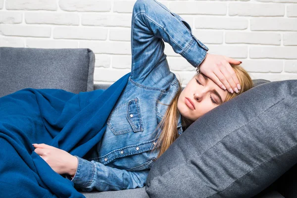 Jeune femme malade fait une sieste sur le canapé, câliné avec une couverture et — Photo