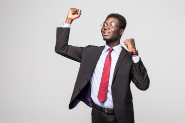Very excited African business man with raised hands in the air isolated grey background clipart
